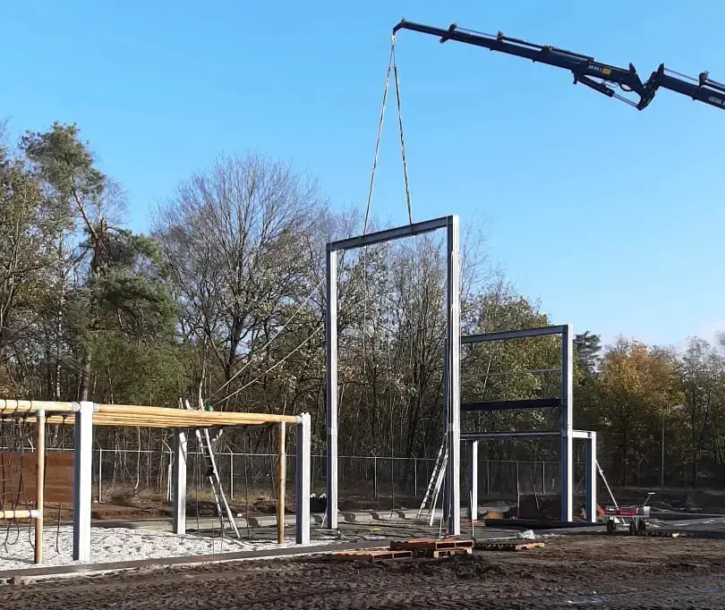 De plaatsing van de staalconstructie voor een survivalrunbaan met behulp van een hijskraan.